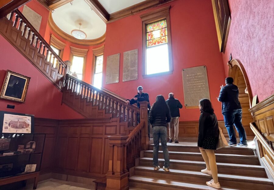 Students in a large house walking up a long staircase with a red wall behind it