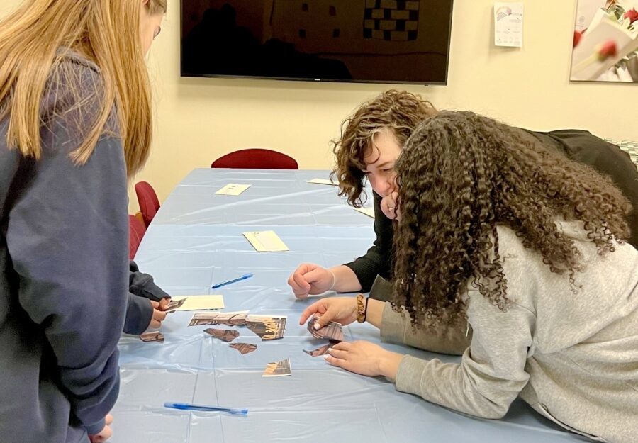 three people leaning over a table piecing paper together