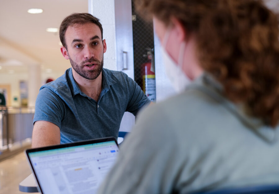 male sitting at a table looking at a female across the table; a laptop is on the table between them