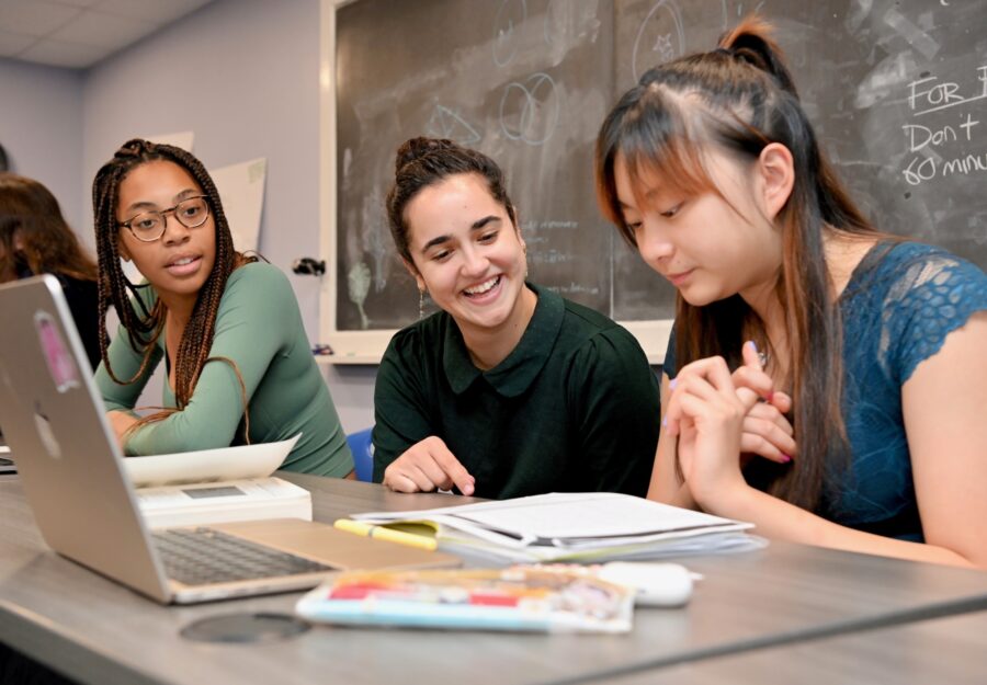female teacher sitting at a table with a student; she is smiling; there is a notebook open on the table