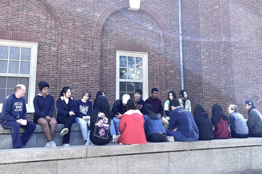 20 students and faculty sit outside near a brick wall