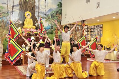 A group of Vietnamese boys performs in a temple. They are wearing white shirts and golden pants.