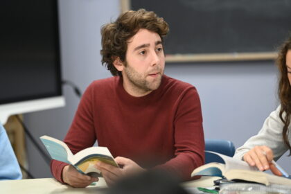 a Caucasian man sitting at a table holding an open book