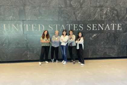 five people stand with arms crossed in front of "United States Senate" sign