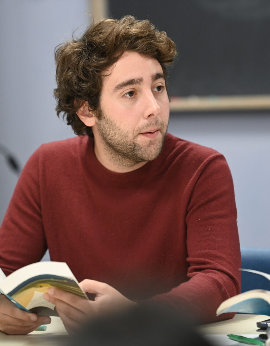 a Caucasian man sitting at a table holding an open book