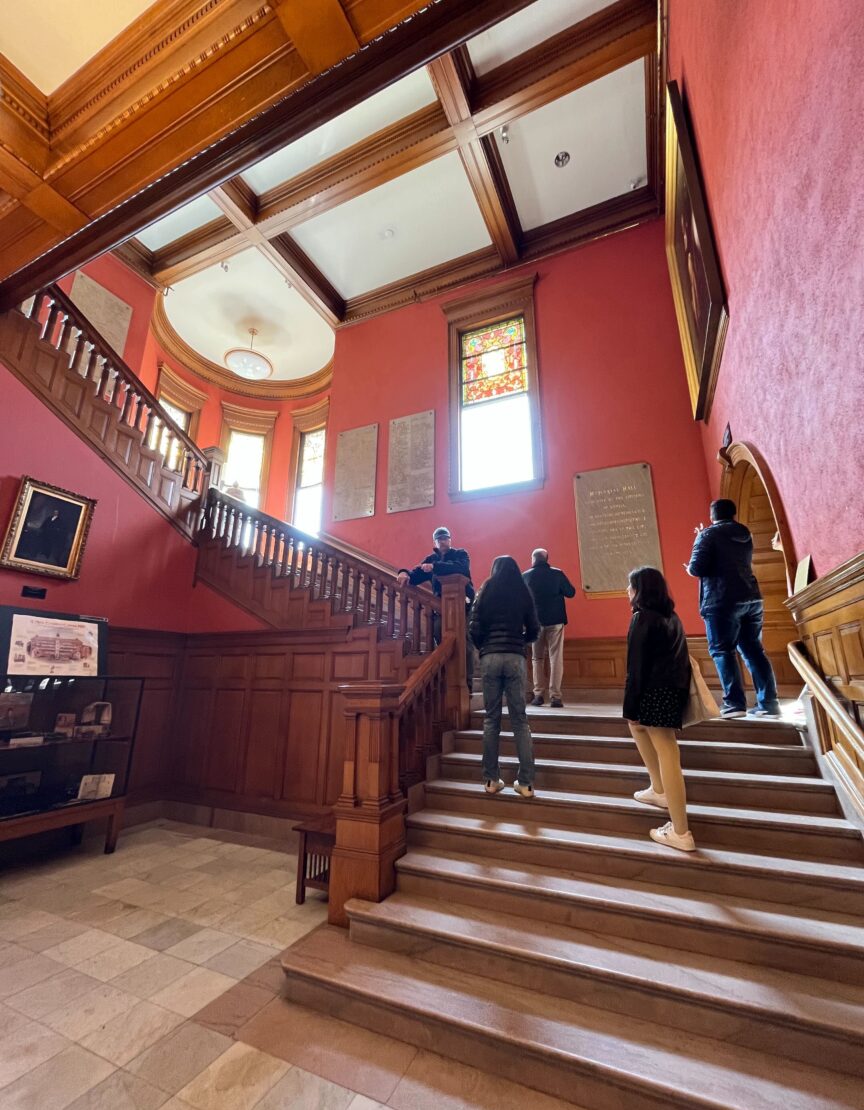 Students in a large house walking up a long staircase with a red wall behind it