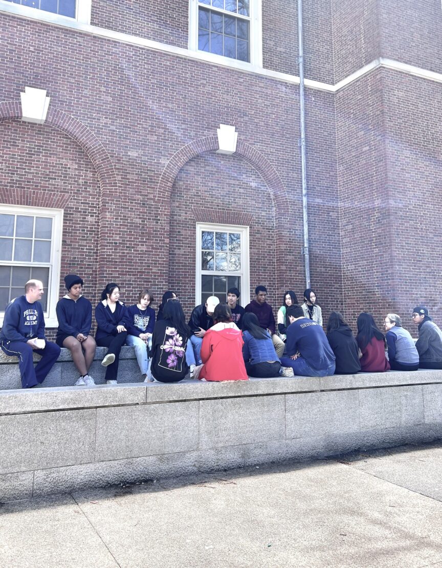 20 students and faculty sit outside near a brick wall